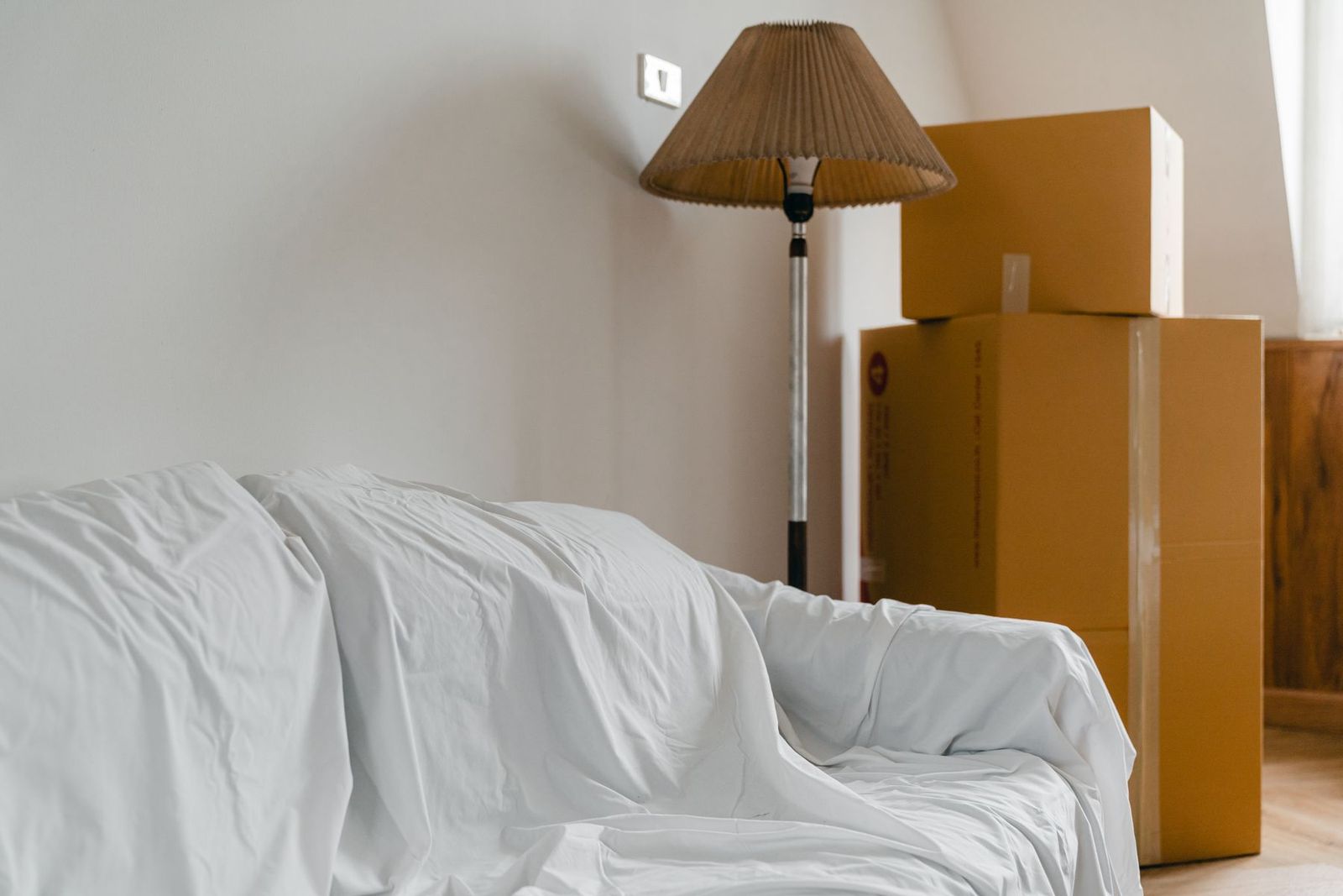 Mit einem Tuch abgedecktes Sofa, Stehlampe und gepackte Kartons in einer leeren Wohnung