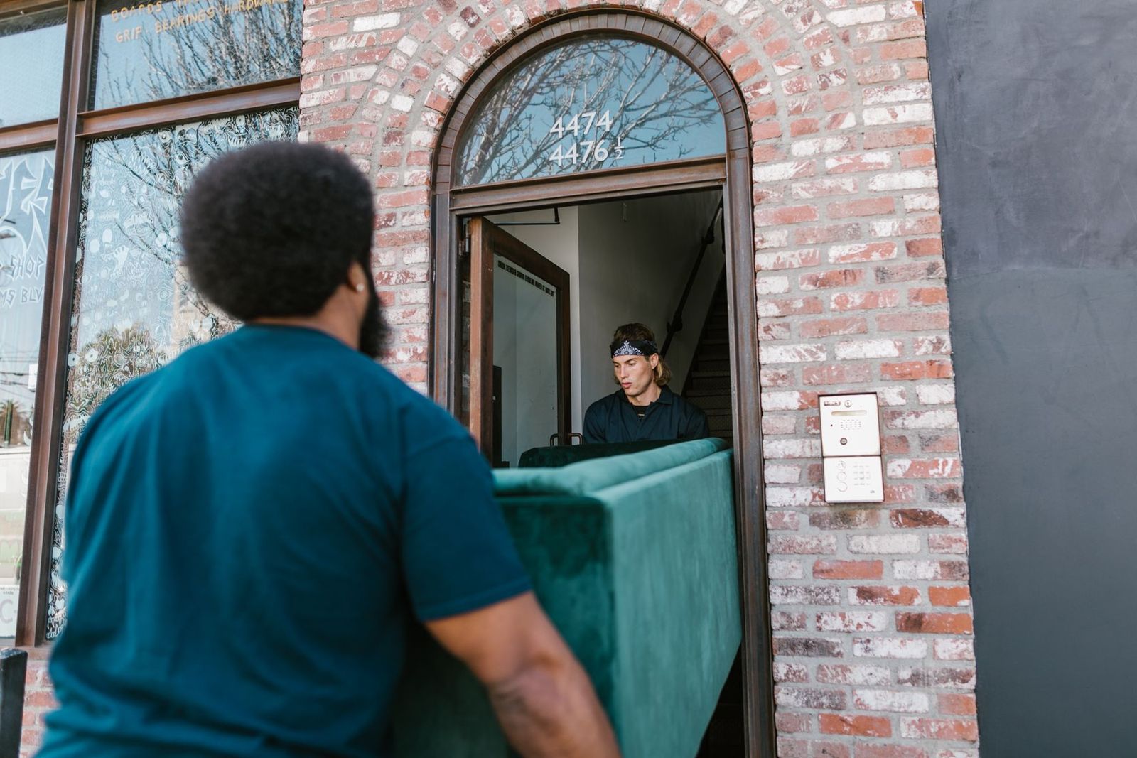 Zwei Männer tragen ein grünes Sofa durch eine Backsteintür ins neue Zuhause